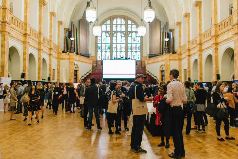 Delegates networking in the Great Hall in front of a screen