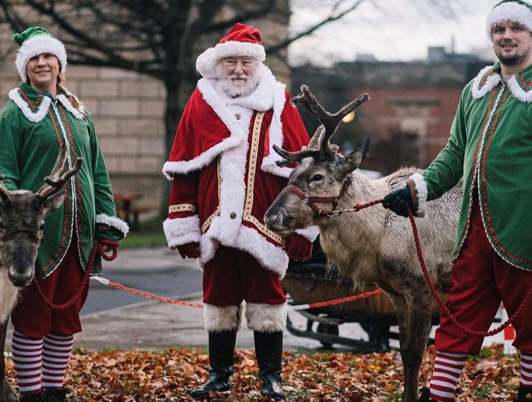 Santa Claus on campus in between two elves and reindeer.