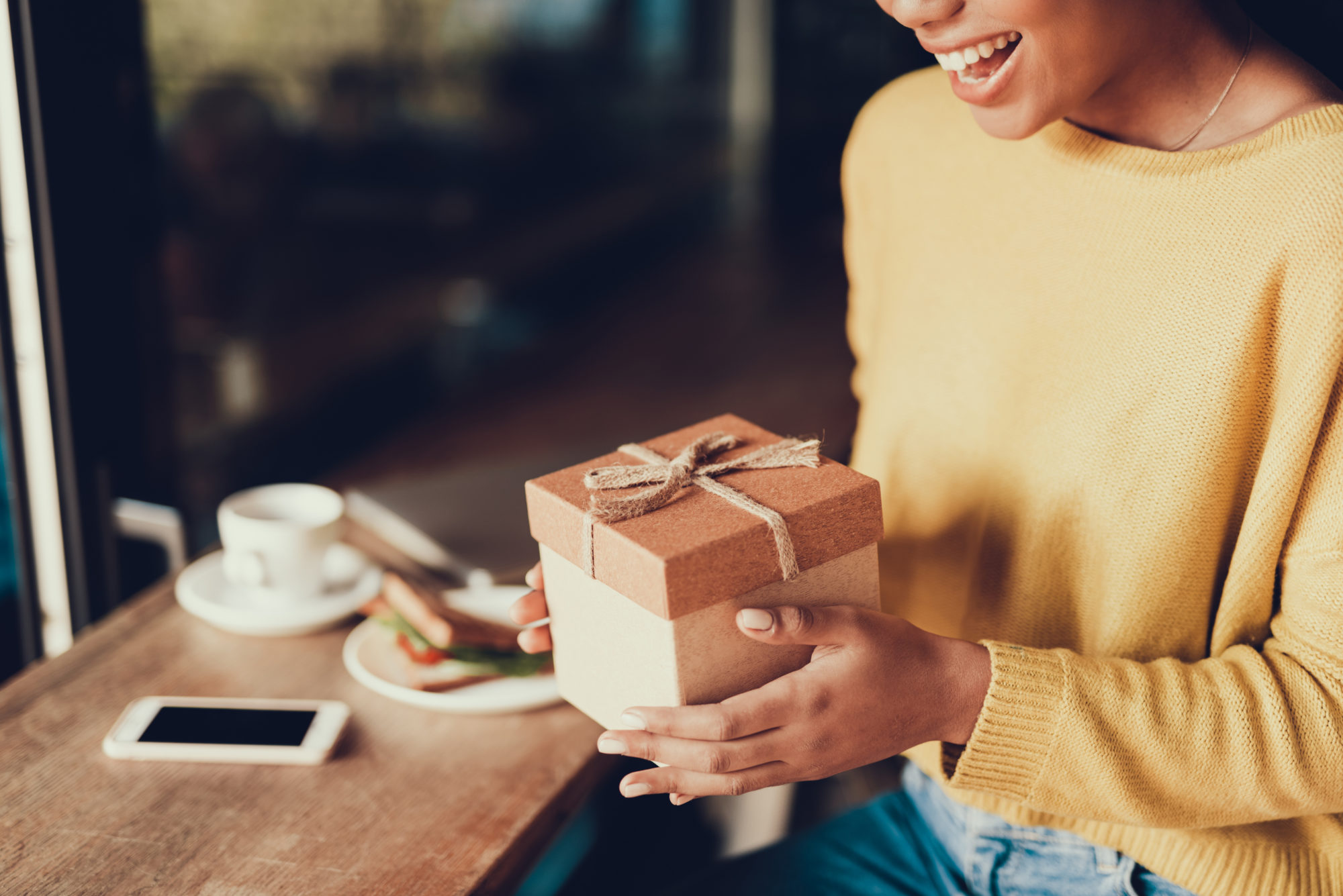 Young woman in yellow jumper holding gift box in hands.
