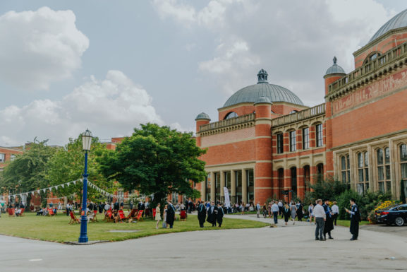 Exterior of the Bramall Music Building on graduation day. Graduates congregate out the front of building in the sun.