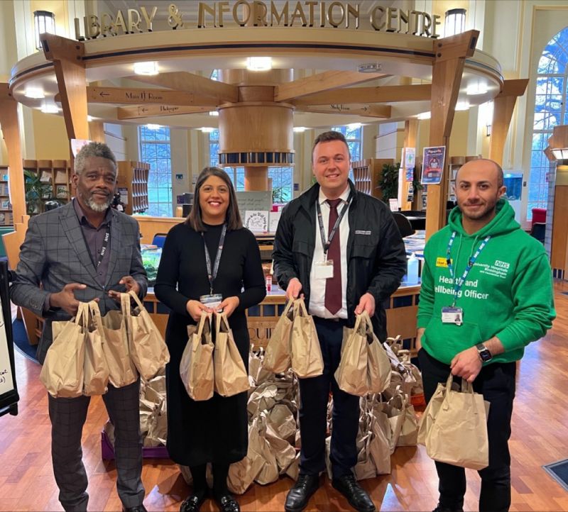 Four people smiling while holding paper bags filled with donated breakfasts for NHS staff.